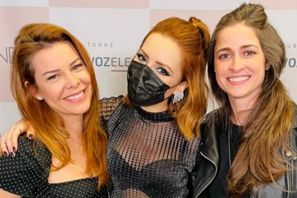 Fernanda Souza de tomara que caia preta, Sandy de máscara de proteção preta e Eduarda Porto,de preto, as três abraçadas