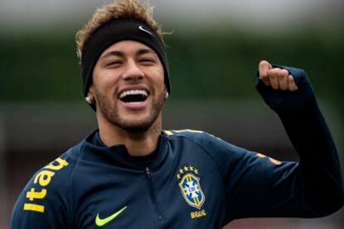 Neymar sorrindo, com casaco da seleção brasileira, dando soco no ar