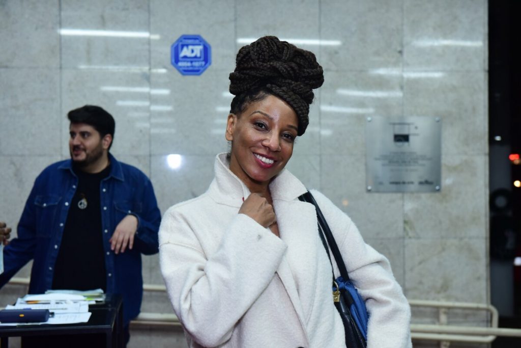 Adriana Lessa de sobretudo branco e tranças no cabelo, sorrindo