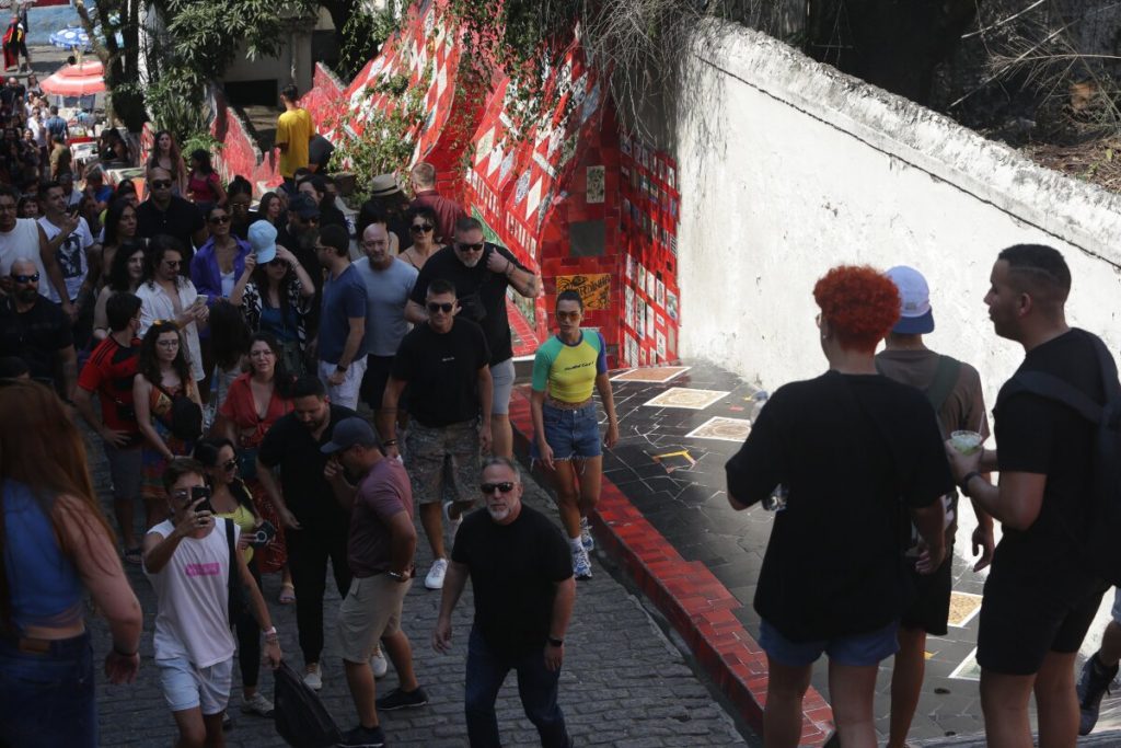 Dua Lipa com camisa verde e amarela, bermuda jeans, no meio da multidão, na escadaria Selaron, na Lapa, RJ