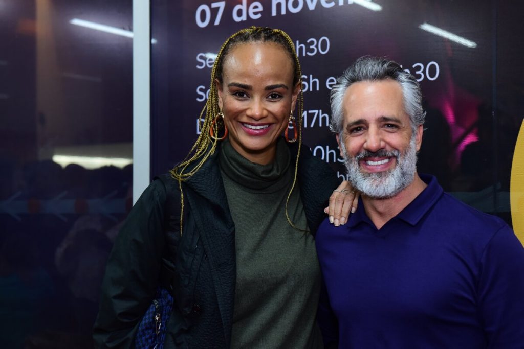 Luciana Melo de verde e preto, com tranças no cabelo,  abraçada ao marido, de azul