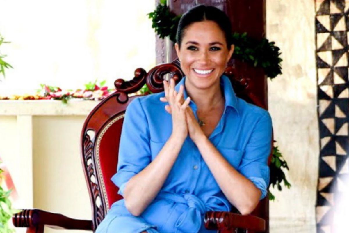 Meghan Markle sorrindo e sentada em uma cadeira