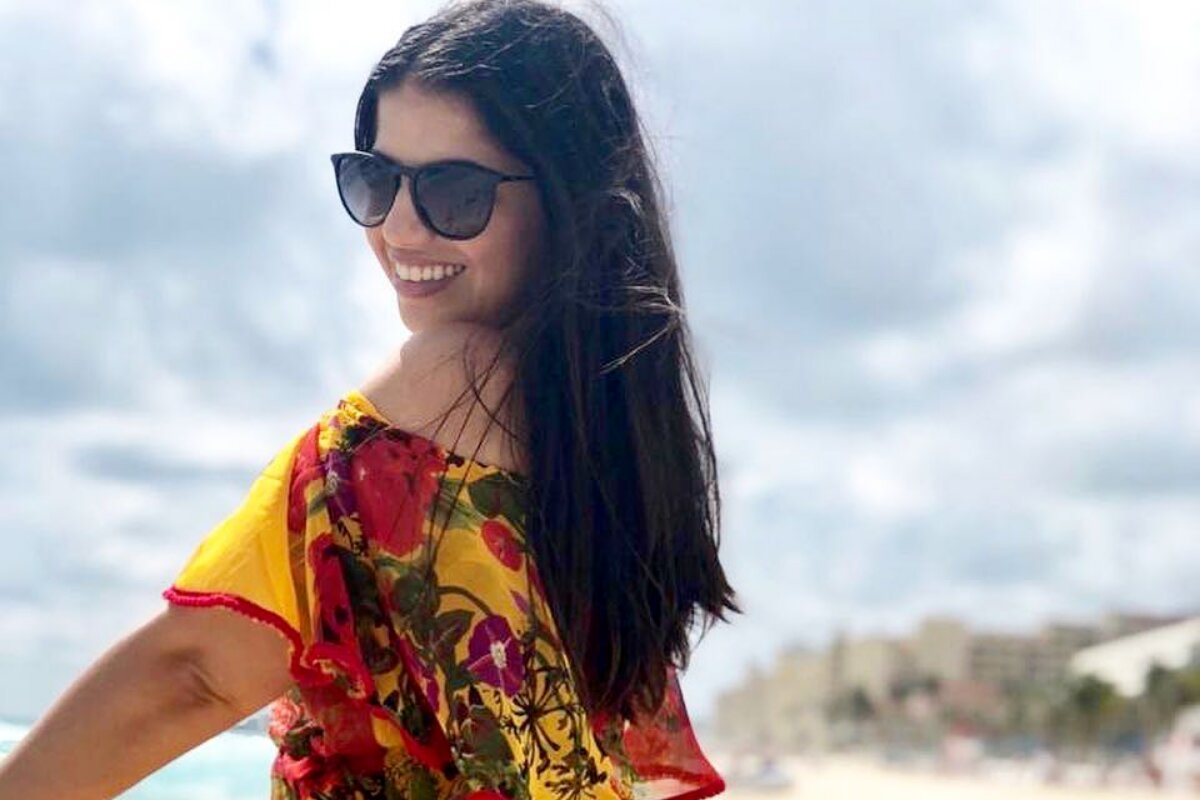 Natalia Soutto de óculos escuros e vestido amarelo e vermelho, sorrindo