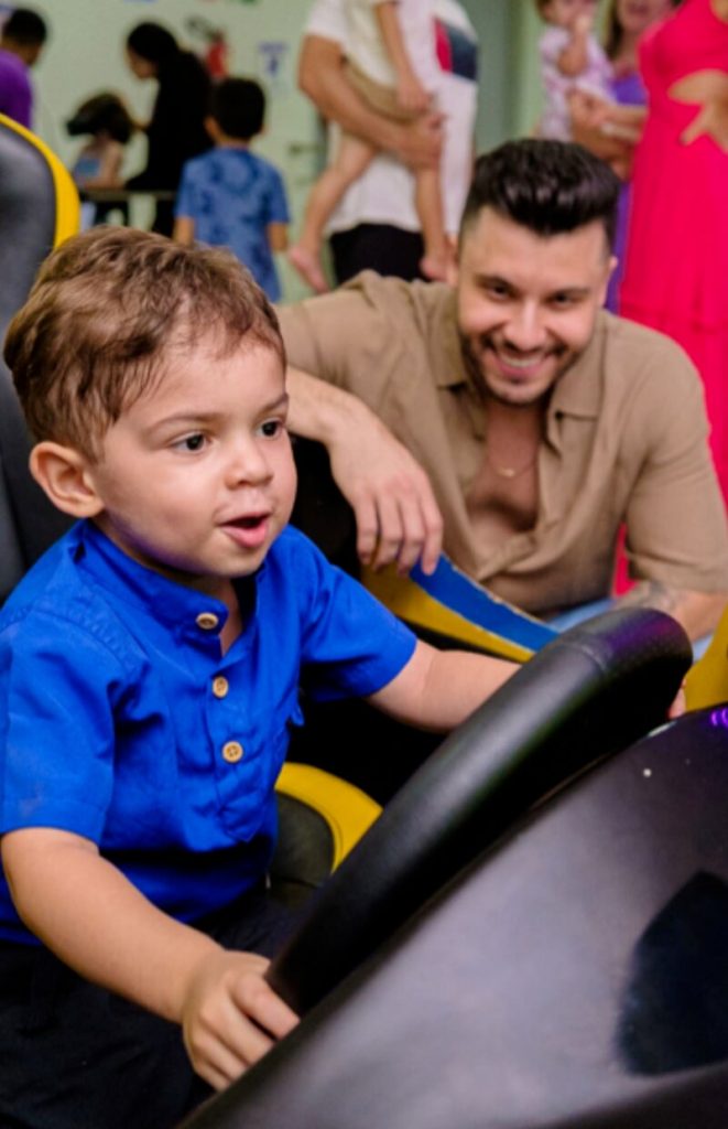 Leo de camisa azul, brincando no carrinho sob olhares do pai, Murilo Huff