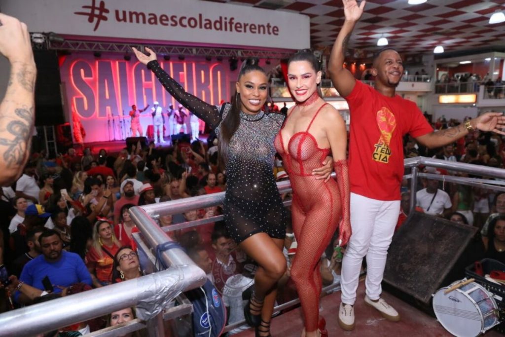 MC Rebeca de vestido preto e Deborah Secco de macacão de tela vermelha na quadra do Salgueiro