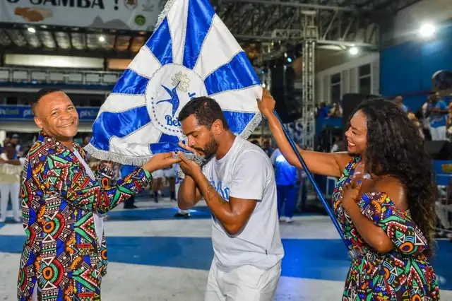 Carnaval 2024 - Samuel de Assis beijando a bandeira da escola de samba Beija-Flor, com o casal de mestre-sala e porta-bandeira